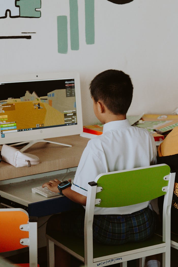 Young boy in school uniform playing computer games in a classroom environment.