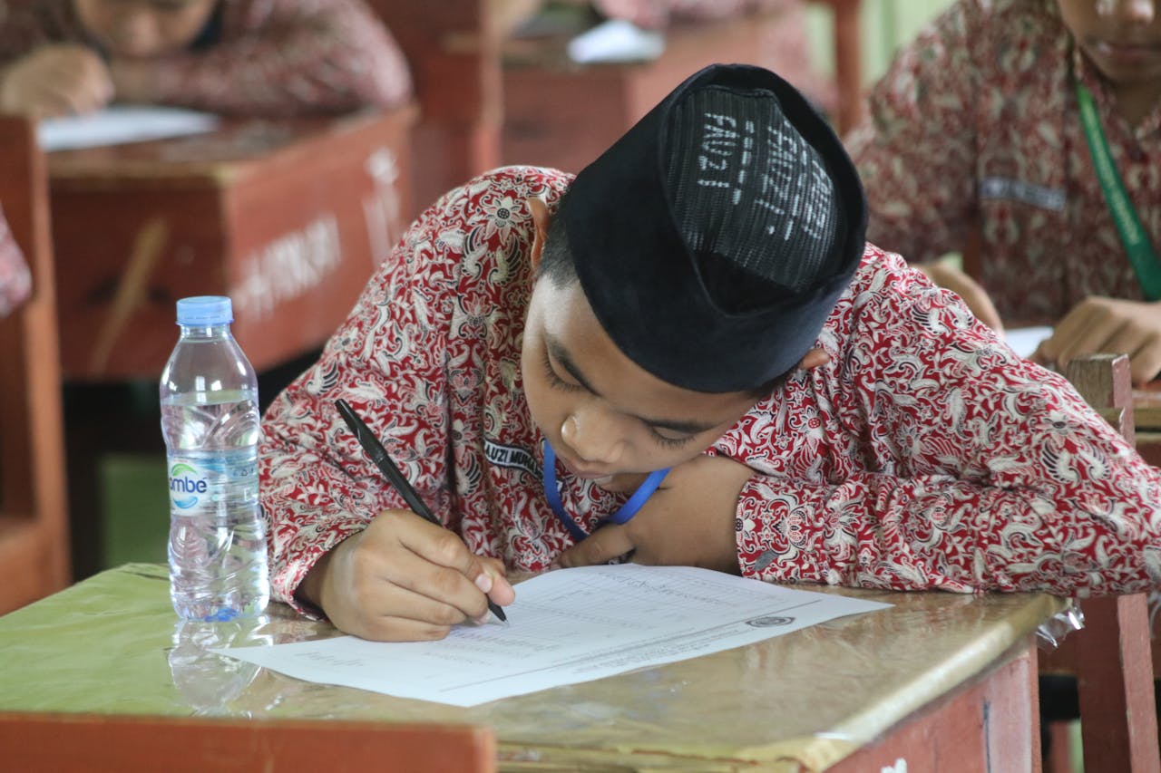 A student in traditional clothing focused on writing an exam at school.