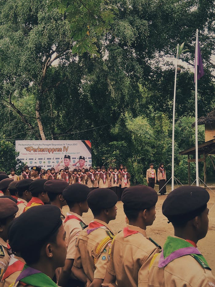 Students in uniform participating in an outdoor school ceremony surrounded by green trees.